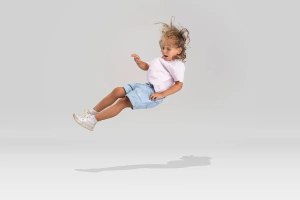 Estúdio tiro de pequena menina caucasiana pré-escolar em roupas casuais caindo isolado sobre fundo estúdio branco. — Fotografia de Stock