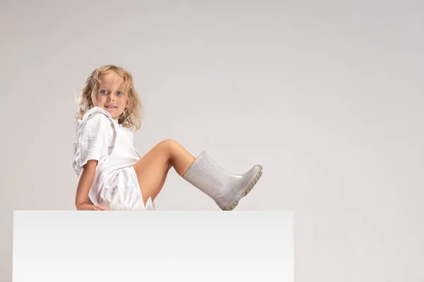 Sidovy porträtt av små söta leende kaukasiska flicka sitter på stor låda isolerad över vit studio bakgrund. — Stockfoto