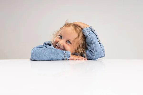 ポートレートの小さな笑顔コーカサス人の女の子でデニム服resting彼女の頭上の手島の上にホワイトスタジオの背景. — ストック写真