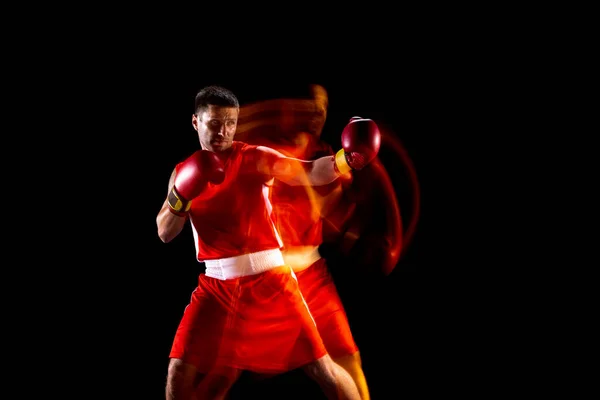 Joven boxeador profesional en pantalones cortos rojos entrenando, ejercitándose sobre fondo negro en luces mixtas — Foto de Stock