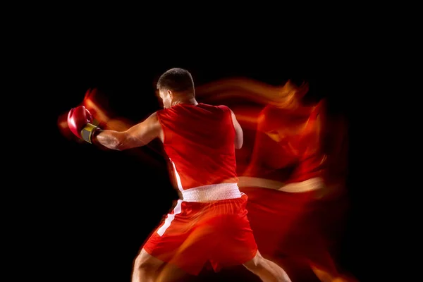 Vista trasera. Un boxeador profesional en pantalones cortos rojos y guantes de entrenamiento, haciendo ejercicio sobre fondo negro en luces mixtas — Foto de Stock