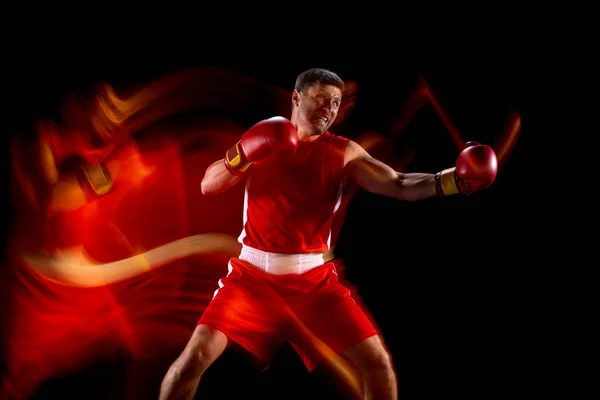 Retrato de boxeador masculino profissional em movimento, ação sobre fundo estúdio preto em luzes mistas. Vista lateral — Fotografia de Stock
