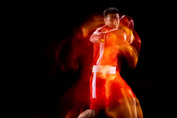 Ütés, kampó. Profi férfi bokszoló portréja mozgásban, akció fekete stúdió háttérrel vegyes fényben. Előnézet — Stock Fotó