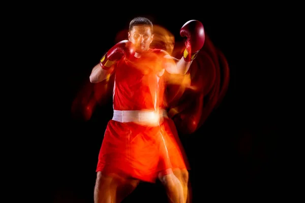 Vista frontal de un boxeador masculino profesional en movimiento, acción sobre fondo de estudio negro en luces mixtas. — Foto de Stock