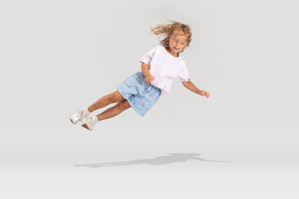 Studio shot of little preschool Caucasian girl in casual clothes falling down isolated over white studio background. Stock Photo