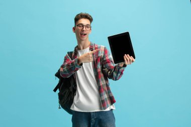 One young caucasian guy, student with backpack and notepad isolated over light blue studio background.