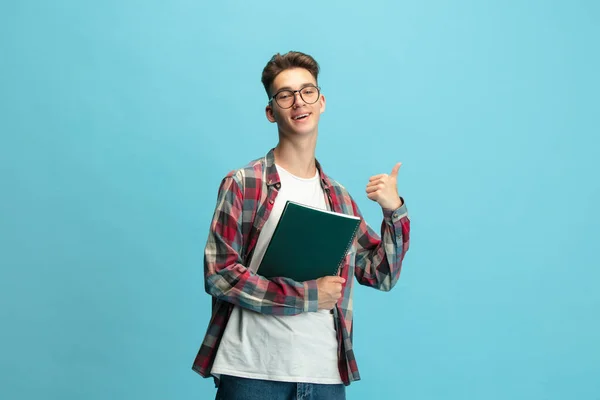 Half length portrait of young caucasian guy, student with notepad isolated over light blue studio background. — Stockfoto