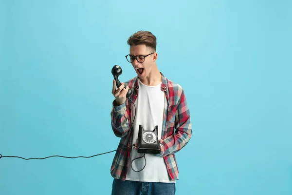 Portrait of young caucasian guy in casual clothes with retro style phone screaming isolated over light blue background. — Stok fotoğraf