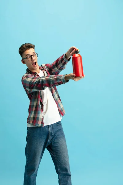 Vertical portrait of young caucasian guy in casual clothes with extinguisher isolated over light blue background. — Stockfoto