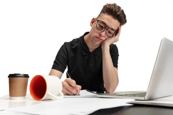 Portrait of one young man, student sitting at table writing or making notes in notepad on white studio background. — Fotografia de Stock