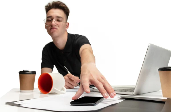 Portrait of one young man, student sitting at table with laptop, cups of coffee and phone on white studio background. — Foto Stock