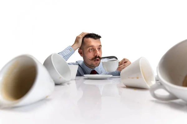 Portrait of young sleepy Caucasian man, office worker sitting at table on white background. — Stock Photo, Image