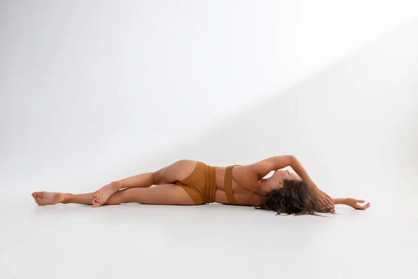 Beyaz arka planda yerde yatan, hardal rengi iç çamaşırlı, bronzlaşmış beyaz bir kadının stüdyo görüntüsü. Arka plan — Stok fotoğraf