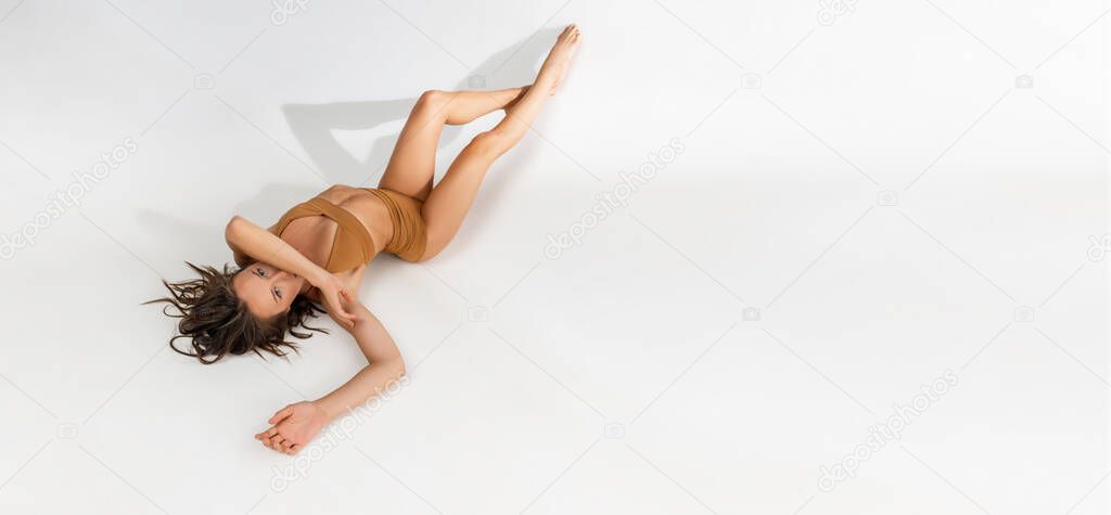 Portrait of young beautiful tanned caucasian woman in mustard underwear lying on floor over white studio background. Flyer