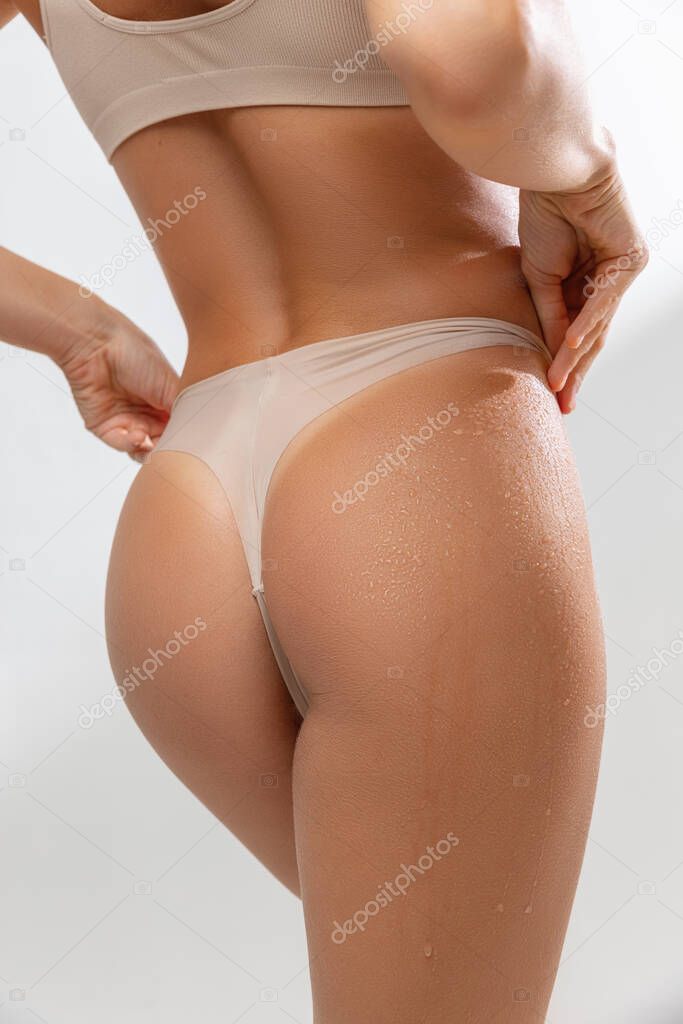 Cropped slim female body in beige underwear standing on white studio background. Back view. Close-up image