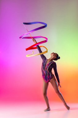 Genç profesyonel bayan ritmik jimnastikçi çok renkli neon arka planda izole edilmiş parlak kurdeleyle egzersiz yapıyor..