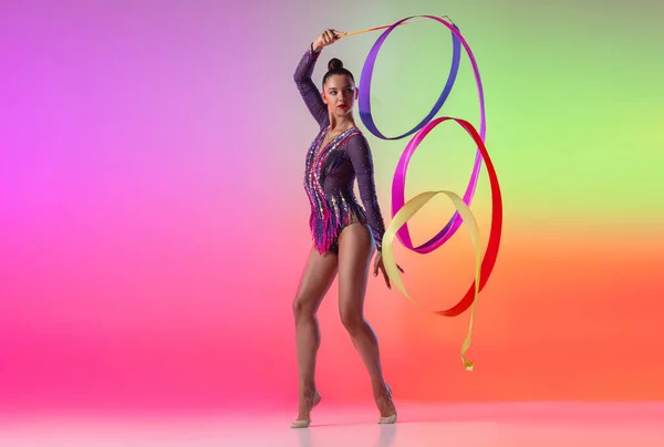 Beautiful young female rhythmic gymnast posing with bright ribbon in her hand isolated on multicolored neon background. — Φωτογραφία Αρχείου