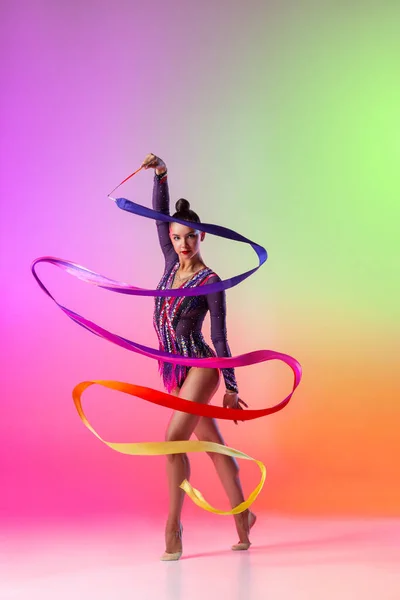아름다운 젊은 여자 리듬 체조 선수가 밝은 리본을 손에 들고 여러 가지 색깔의 네온 배경에 고립되어 있는 모습. — 스톡 사진