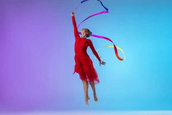 Одна професійна жіноча гімнастка в червоній сукні вправа з яскравою стрічкою ізольована на градієнтному неоновому фоні . — стокове фото