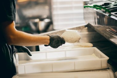 Genç aşçı ekmek hazırlıyor, hamur işlerini restoran mutfağındaki masada yoğuruyor. Yan görünüm.