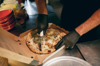 Yakın plan. Şef lezzetli sıcak pizzayı karton bir kutuda parçalara ayırıyor. Lezzetli ve aromatik görünüyor.