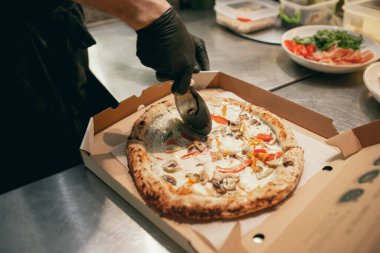 Yakın plan. Şef lezzetli sıcak pizzayı karton bir kutuda parçalara ayırıyor. Lezzetli ve aromatik görünüyor.