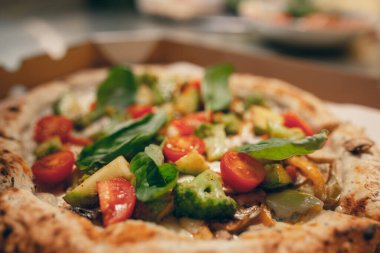 Lezzetli görünüyor, lezzetli. Karton kutuda domatesli, kabaklı, mantarlı ve brokolili lezzetli vejetaryen pizzanın yakın plan görüntüsü..