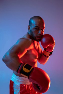 Yakın plan. Kırmızı eldiven eğitiminde profesyonel bir boksör, mor arka planda neon ışıkta egzersiz yapıyor..