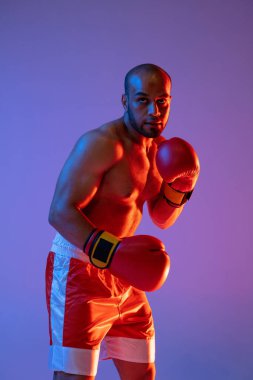 Kırmızı eldiven eğitimi almış bir profesyonel boksörün dikey görüntüsü. Mor arkaplanda izole edilmiş bir şekilde neon ışığı altında egzersiz yapıyor..