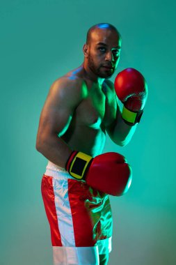 Yakın plan. Kırmızı eldivenli profesyonel bir boksör mavi yeşil arka planda neon ışıkta egzersiz yapıyor..