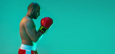 Yan görüş. Profesyonel bir boksör, elleri mavi yeşil arka planda, neon ışıkta yan yana duruyor. El ilanı