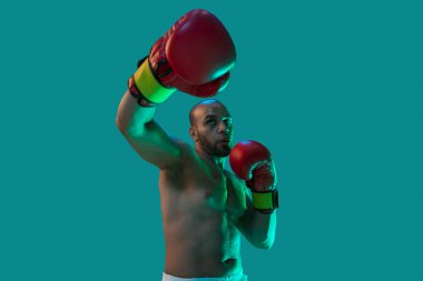 Güçlü yumruklar. Kırmızı şortlu profesyonel bir boksör, neon ışıklı mavi arka planda izole edilmiş egzersiz yapıyor..