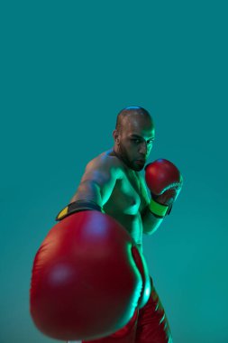 Yakın plan. Kırmızı şortlu profesyonel bir boksör, neon ışıklı mavi arka planda izole edilmiş egzersiz yapıyor..