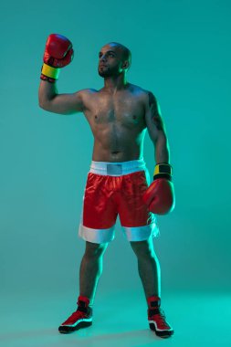 Bir profesyonel erkek boksörün dikey portresi mavi yeşil arka planda, neon ışıkta tek başına duruyor..