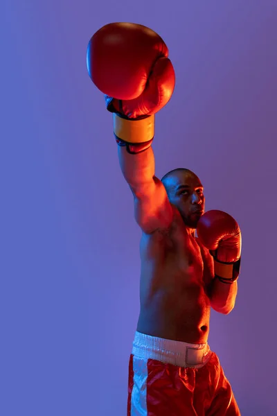 Starke Fäuste. Ein Profiboxer beim Training in roten Shorts, der isoliert auf lila Hintergrund in Neonlicht trainiert. — Stockfoto