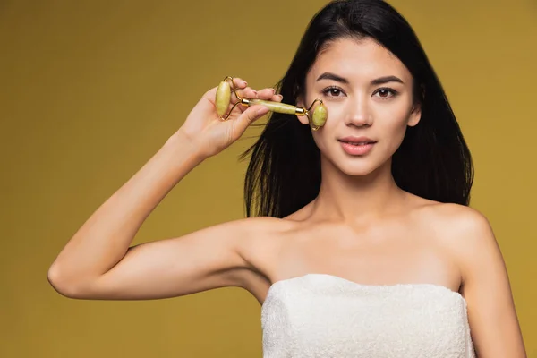 Studio image of beautiful young woman with face roller looking at camera.