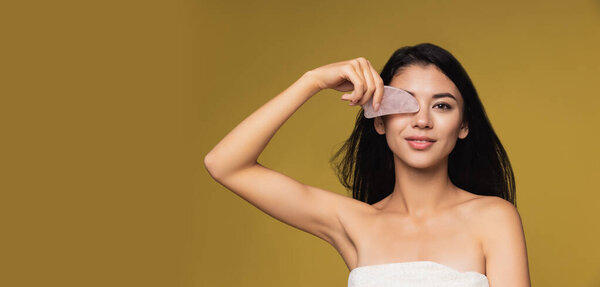 Studio image of beautiful young woman with gua sha stone looking at camera. Flyer