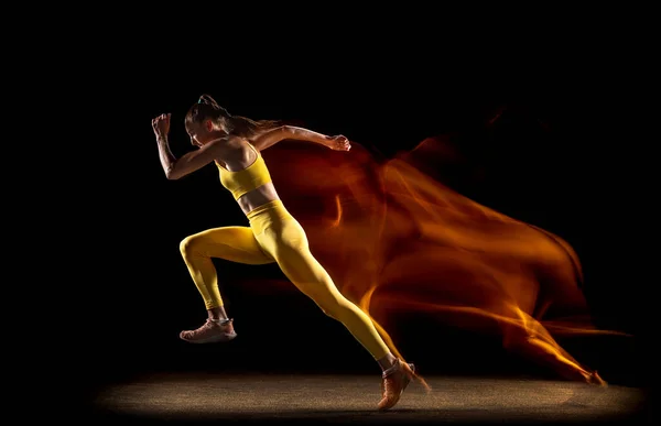 Jovem, atleta feminina treinando isolado sobre fundo estúdio preto em luzes de néon mistas. Vista lateral — Fotografia de Stock