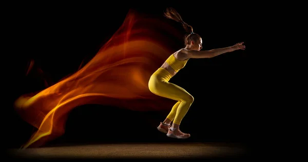 O Flyer. Jovem, atleta feminina treinando isolado sobre fundo estúdio preto em luzes de néon mistas. Vista lateral — Fotografia de Stock