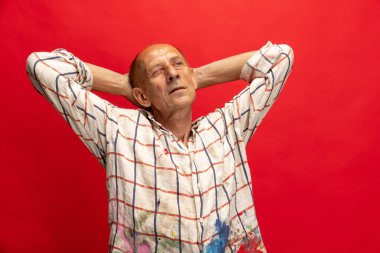 Olgun ya da yaşlı gri boyacı elinde fırçayla kameranın önünde duruyor. Boya lekeli gömlekli komik bir adam. Kırmızıda izole bir şekilde oyalanıyor.