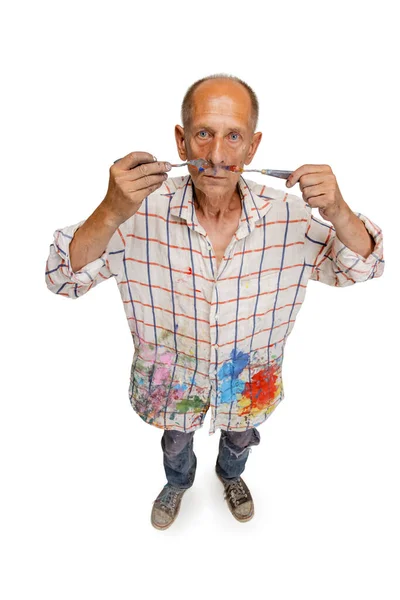 Peintre mature ou senior gris avec un pinceau debout devant la caméra. Homme drôle dans une chemise teintée de peinture s'amuser autour isolé sur blanc — Photo