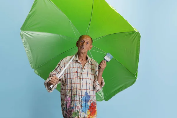 Pintor gris maduro o senior con un pincel delante de la cámara. Hombre gracioso en una camisa manchada de pintura tonteando —  Fotos de Stock