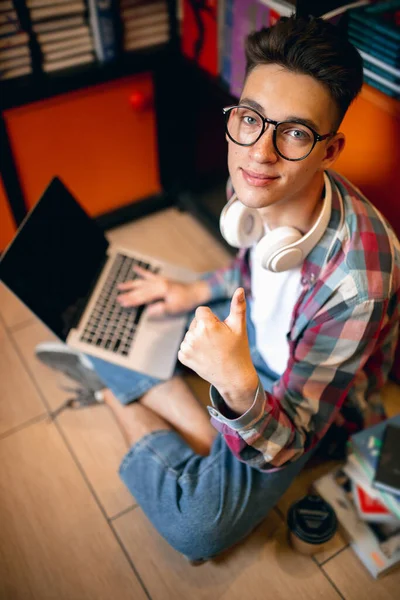 Un giovane ragazzo caucasico, studente seduto al piano con computer portatile su sfondo casa o biblioteca. — Foto Stock