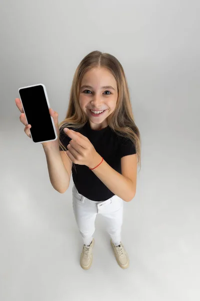 Showing device screen. One little screaming school girl holding smartphone isolated over white studio background. — Stock Photo, Image