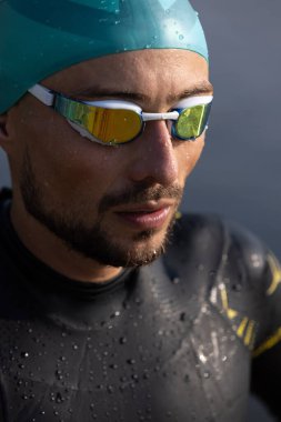 Nehirlerde yüzmeden önce profesyonel triatloncu. Yüzme ekipmanı giyen bir adam yaz günlerinde plajda triatlon antrenmanı yapıyor..