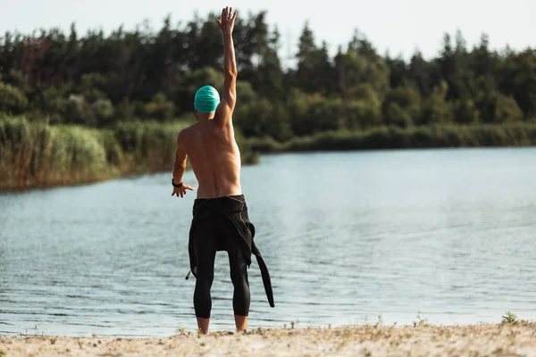 川のオープンウォーターで泳ぐ前にプロの選手。夏の日にビーチでトライアスロンを練習する水泳用具を身に着けている男. — ストック写真
