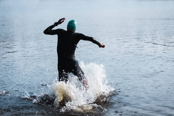 Professional triathlete swimming in rivers open water. Man wearing swim equipment practicing triathlon on the beach in summers day.