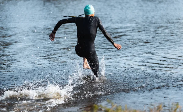Professional triathlete swimming in rivers open water. Man wearing swim equipment practicing triathlon on the beach in summers day.