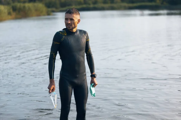 川のオープンウォーターで泳ぐ前にプロの選手。夏の日にビーチでトライアスロンを練習する水泳用具を身に着けている男. — ストック写真