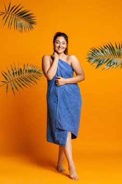 Büyük banyo havlusuyla sevimli, tombul bir kadın turuncu stüdyo arka planında izole edilmiş..